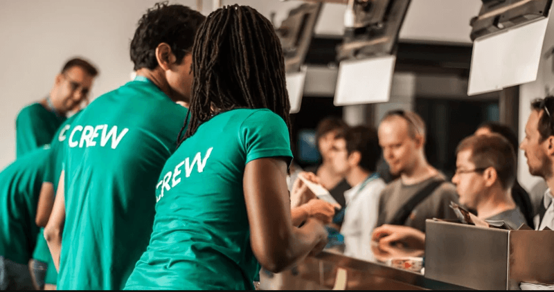 AAMP Agency - 4 Ways to Build Brand Reputation and Recognition 7 Event staff in green 'CREW' t-shirts assisting attendees at a registration desk.