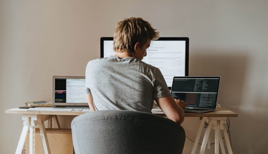 Person working at a desk with multiple computer screens, multitasking in a home office setting.