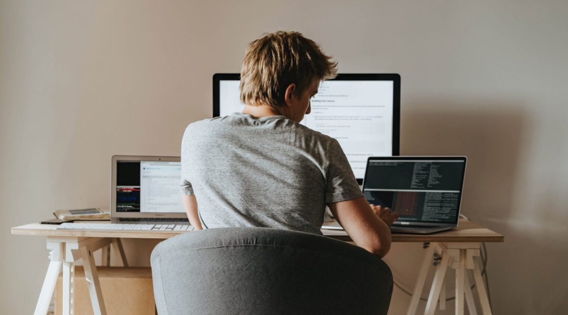 Person working at a desk with multiple computer screens, multitasking in a home office setting.