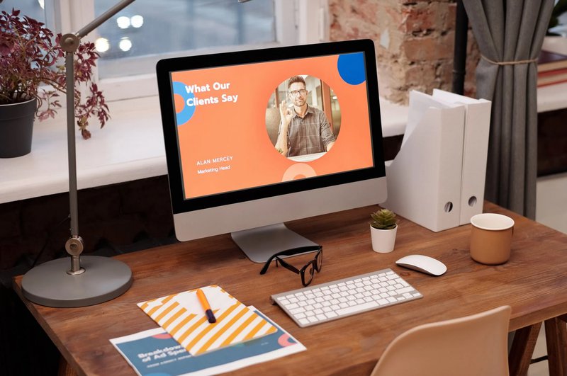 Modern workspace with computer displaying testimonials, a desk lamp, plant, and office supplies.