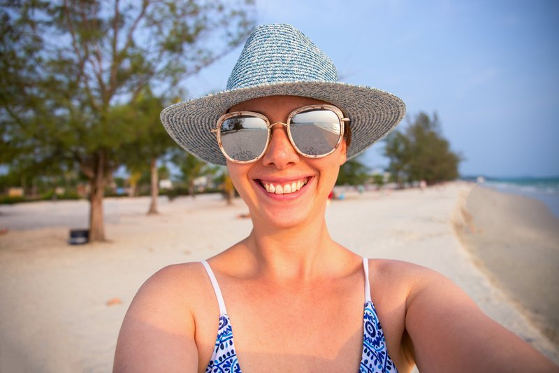 Person in a sun hat and swimsuit at a beach with trees and sand.
