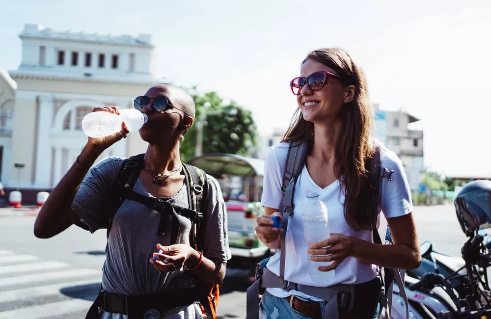 Two people holding water bottles on a sunny day, standing in front of motorcycles.