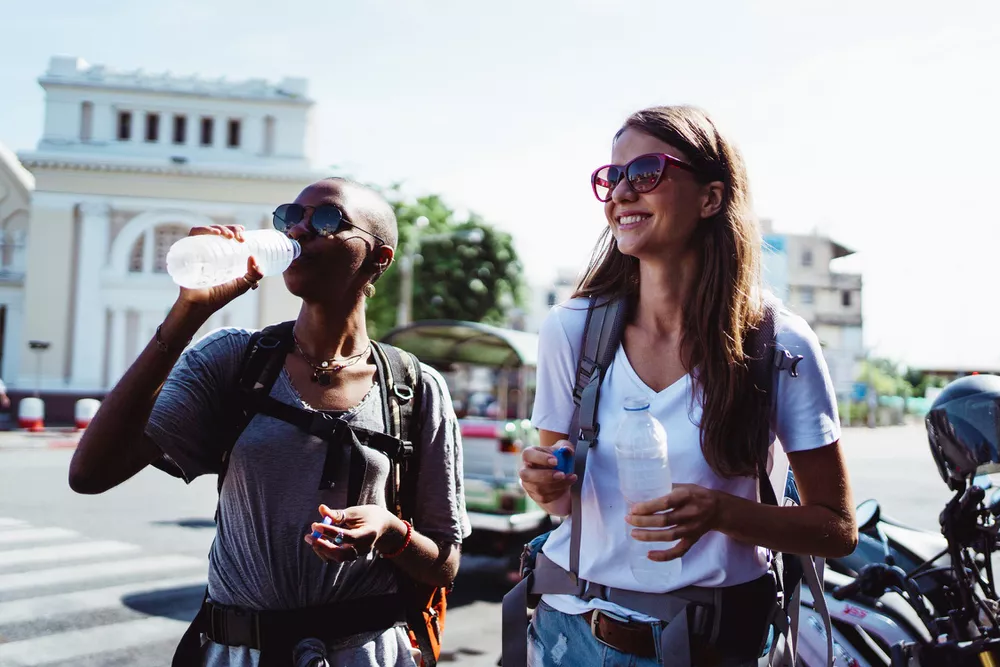 Two people holding water bottles on a sunny day, standing in front of motorcycles.
