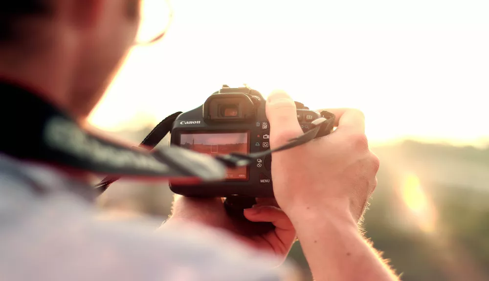 Person holding a Canon DSLR camera focusing during a bright sunset.