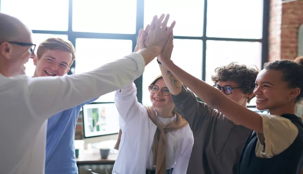 Group of individuals giving a high-five in a bright office setting.
