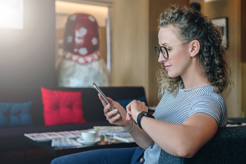 Person sitting and using a smartphone in a cozy room with a coffee table and red pillow.