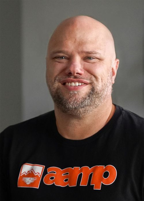 a person in a black t-shirt with orange logo, standing against a grey background.