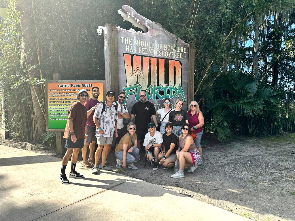 Aamp team posing beside a 'Wild Florida' sign at a tropical park entrance.