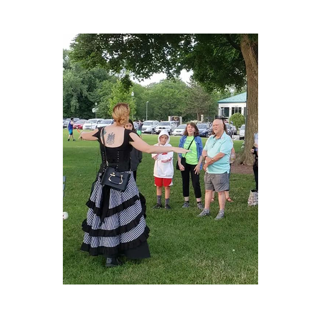 An American Ghost Walks guide in a Victorian dress telling a story to a tour group in a park
